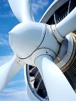 Close-up view of white aircraft propeller blades and engine hub against blue sky with clouds, showcasing modern aviation technology and aerodynamic design.