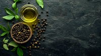 Fresh black peppercorns in wooden bowl with olive oil and green basil leaves on dark stone background. Food ingredients composition with copy space.
