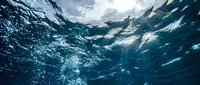 Underwater view of ocean waves with sunlight filtering through deep blue water creating dynamic patterns and bubbles for marine and aquatic themes.