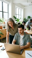 Mature woman with gray hair and Hispanic male colleague collaborating at laptop in bright office with plants, teamwork and mentoring concept.