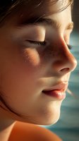 Close-up profile of young Asian woman with closed eyes in warm sunlight showing natural freckles, flawless skin and serene expression against blurred background.