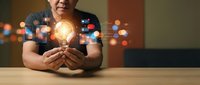 Senior Asian man holding glowing light bulb with digital icons, symbolizing innovation, creativity, and smart technology solutions in modern business.