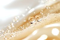 Golden wedding rings with water drops on silky beige fabric creating romantic bokeh effect, macro photography for wedding and engagement announcements.