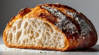 Freshly baked artisan sourdough bread with crispy golden crust and airy honeycomb crumb structure, cut to show texture on gray background.
