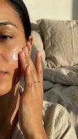 Young Middle Eastern woman applying face cream in warm sunlight, morning skincare routine at home, healthy glow, natural beauty concept.