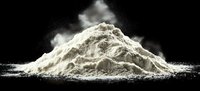 White flour or powder pile with dramatic cloud of dust against black background, creating contrast and dynamic composition for culinary or baking concepts.