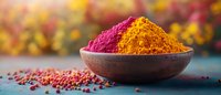 Vibrant pink and yellow spice powders in rustic clay bowl with scattered peppercorns on dark surface against colorful blurred background, panoramic food composition.