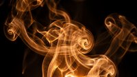 Abstract golden orange smoke swirls dancing against black background creating elegant flowing patterns for luxury design projects.