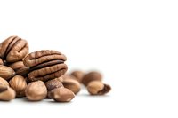 Fresh pecan nuts and hazelnuts scattered on white background, close-up macro shot with selective focus and copy space for text placement.