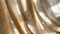 Sunlight streaming through sheer beige curtains creates soft shadows and folds, adding depth and ethereal atmosphere to minimal interior design element.
