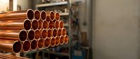 Stack of shiny copper pipes in industrial warehouse storage facility for plumbing construction and manufacturing applications.