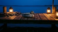 Peaceful evening scene with lanterns illuminating wooden dock over calm blue water. Serene lakeside atmosphere perfect for relaxation and tranquility concepts.