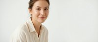 Young professional Asian woman in white shirt smiling confidently at camera against neutral background for business and corporate presentations.