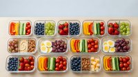 Healthy meal prep containers with fresh fruits, vegetables, nuts and boiled eggs arranged in organized lunch boxes for balanced nutrition and diet planning.
