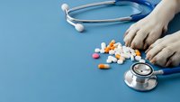 Healthcare professional hands with stethoscope and colorful medication pills on blue medical background for pharmacy and treatment concepts.