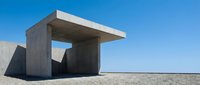 Modern concrete bus shelter with minimalist architectural design on empty desert landscape under clear blue sky.