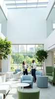 Modern office lobby with diverse businesspeople meeting in bright atrium space with natural light, contemporary furniture and urban skyline view.