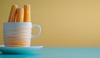 Spanish churros served in white ceramic cup on turquoise table against golden background, minimalist food photography composition for cafe menu or dessert blog.