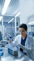 Female scientist in safety glasses using pipette in modern laboratory conducting research experiments with test tubes and equipment.
