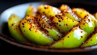 Fresh green mango slices seasoned with chili powder and spices on dark plate, close up view showing vibrant colors and texture of tropical fruit snack.