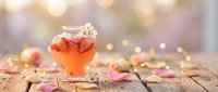 Warm autumn tea in glass mug with apple slices on rustic wooden table surrounded by colorful fall leaves and soft bokeh lights for cozy seasonal atmosphere.