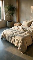 Serene bedroom interior with unmade beige linen bedding, potted olive tree by window, wooden nightstand, and neutral earth-tone walls creating a minimalist, calming sanctuary for relaxation and sleep.