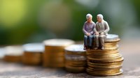 Senior couple figurines sitting on stack of gold coins, representing retirement savings, pension funds and financial planning for elderly care. Blurred background.