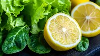Fresh green leafy vegetables with sliced lemon on dark surface for healthy cooking and salad preparation.
