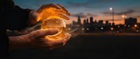 Young adult male hands holding glowing crystal ball with illuminated cityscape at dusk in background, symbolizing future vision, business forecasting, and strategic planning concepts.
