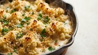 Creamy baked cauliflower gratin with golden cheese crust and fresh herbs in cast iron skillet, comfort food side dish for family dinner and holiday meals.