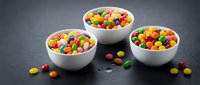 Colorful candy-coated chocolates in white ceramic bowls on dark slate surface for confectionery marketing and sweet treat advertising campaigns.