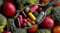 Colorful dietary supplements and vitamin pills on vintage spoon with fresh vegetables and fruits in background, promoting healthy nutrition concept.