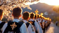 Young men in traditional religious attire with embroidered crosses stand in line during sunset ceremony, backlit by golden light through cherry blossoms against mountain backdrop.