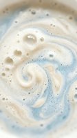 Creamy swirled foam texture with blue and beige tones creating abstract patterns. Soap bubbles and frothy surface for skincare and beauty concepts.