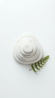 Concentric white ceramic bowls arranged in spiral formation with fresh green fern leaf on neutral background, isolated for design and branding projects.