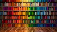 Colorful rainbow bookshelf wall with organized books arranged by color spectrum from red to purple on wooden floor for library and education concepts.