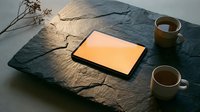 Tablet with blank yellow screen on slate surface with coffee cups and dried flowers for web design and digital product mockup.