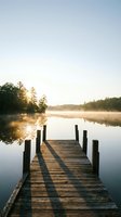 Wooden dock extending into calm lake at sunrise with mist rising from water and forested shoreline, suitable for nature, travel, and wellness marketing.