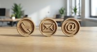 Wooden contact icons on office desk featuring phone, email and at symbol for business communication and customer service concepts.