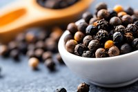 Mixed black and white peppercorns in ceramic bowl on dark background, selective focus on aromatic spices for cooking and seasoning.