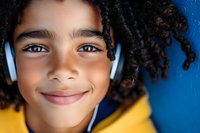 Close up portrait of smiling African American child with curly hair wearing blue headphones against vibrant blue and yellow background, expressing joy and happiness.