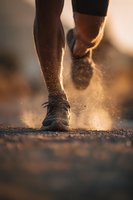 Runner's legs in motion kicking up dust on dirt trail during outdoor workout. Dynamic action shot capturing athletic movement and endurance training.