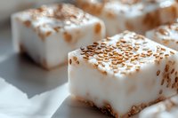 Creamy white marshmallow squares topped with golden toasted coconut flakes on light background, macro view of homemade dessert confectionery.
