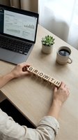 Business professional arranging wooden letter blocks spelling GROWTH on desk with laptop displaying analytics dashboard, coffee cup and succulent plant.