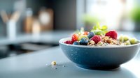 Healthy breakfast bowl with fresh berries, granola and yogurt in blue ceramic dish on kitchen countertop with natural light.