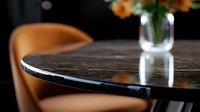 Modern round black marble dining table with orange leather chair and glass vase in background, elegant home interior detail with selective focus.