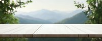 Empty wooden table surface against blurred mountain landscape background with green foliage frame, suitable for product display and digital compositing.