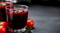 Fresh tomato juice garnished with herbs in glass on dark background with ripe cherry tomatoes, healthy vegetable drink for detox and wellness.