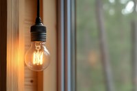 Glowing vintage filament light bulb hanging near window with soft bokeh background, warm atmospheric lighting creates cozy minimalist home ambiance.