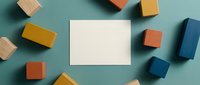 Colorful wooden blocks scattered around blank white card on teal background. Creative workspace mockup for presentations, branding, educational materials.